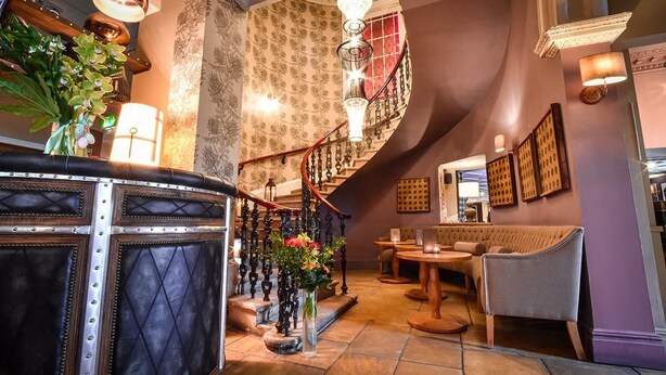 A grand lobby with a staircase, leather seating, and decorative lighting. - The Meadowpark (Stirling)