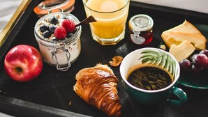 A breakfast tray with a croissant, apple, yogurt with berries, orange juice, cheese, grapes, coffee, and a jar of jam. - The Meadowpark (Stirling)