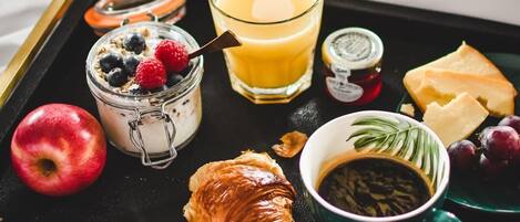 A breakfast tray with a croissant, apple, yogurt with berries, orange juice, cheese, grapes, coffee, and a jar of jam.