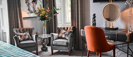A hotel room with two armchairs, a sofa, a desk with a mirror, and a television.