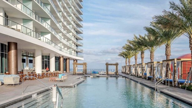 A pool area with a modern building, outdoor seating, and palm trees. - Cozy unit @ 18th Floor with Ocean view (Hollywood)