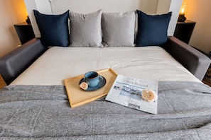 Un lit bien fait, avec un plateau contenant des articles pour le petit-déjeuner, un journal et une lampe sur une table de chevet.