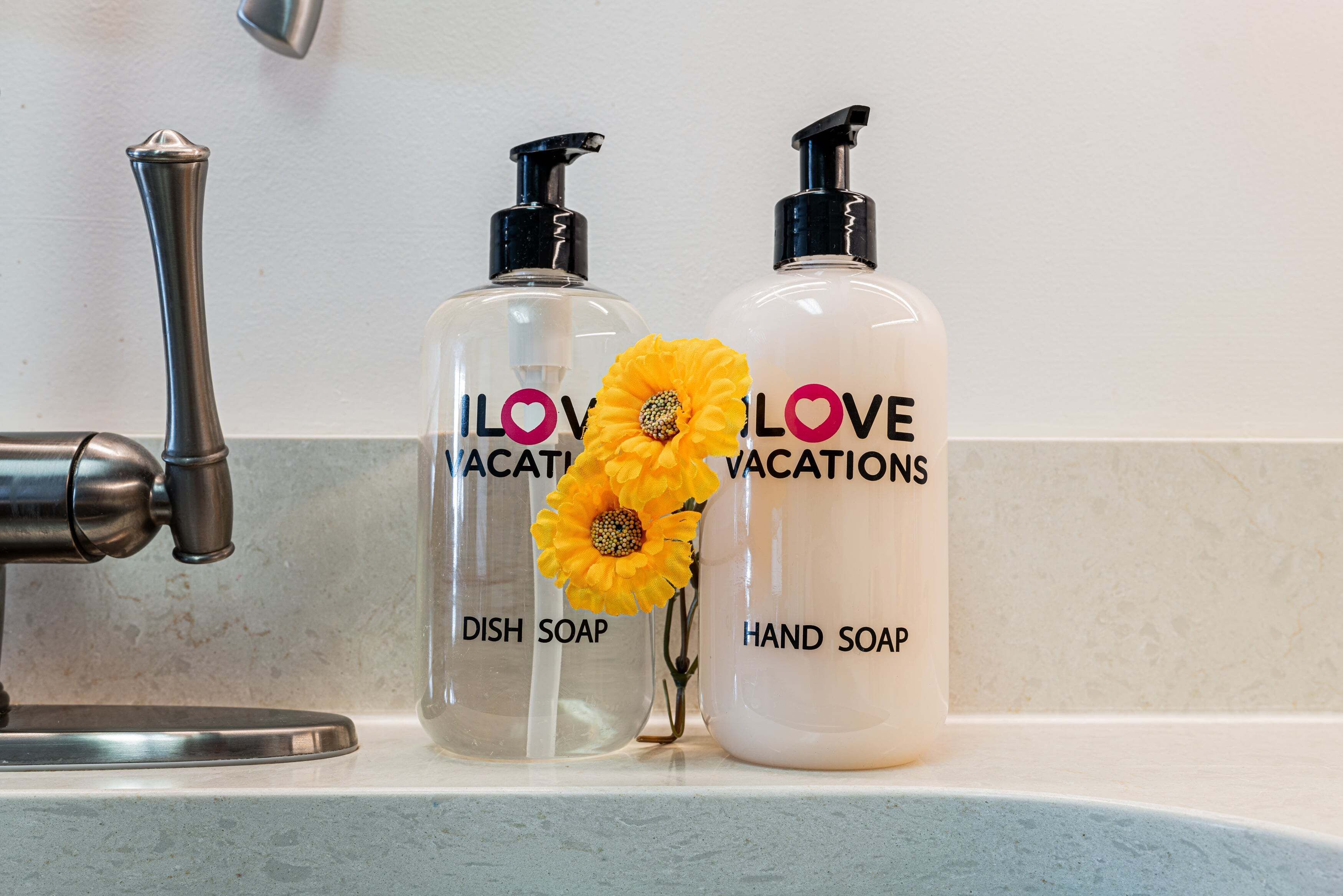Dos botellas de detergente para platos y jabón de manos con una flor sobre una encimera de baño.
