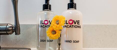 Dos botellas de detergente para platos y jabón de manos con una flor sobre una encimera de baño.