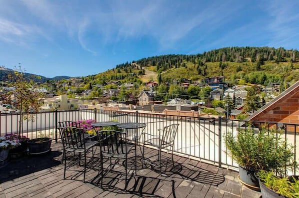 Une terrasse avec des places assises extérieures, une vue sur un village perché sur une colline et un ciel dégagé.