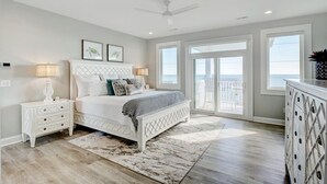 Une chambre à coucher comprenant un lit, des tables de chevet, une commode et donnant sur l’extérieur.