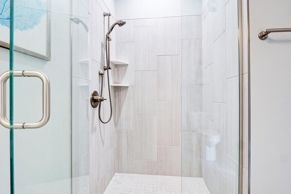 Moderni suihku, jossa on lasiovi, käsisuihkupää ja seinälle kiinnitetty hylly.