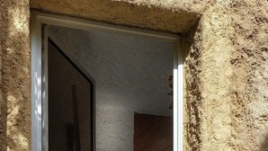 Una puerta que da a un cuarto con vistas al exterior, una escultura de león de piedra y una escalera apoyada en la pared.