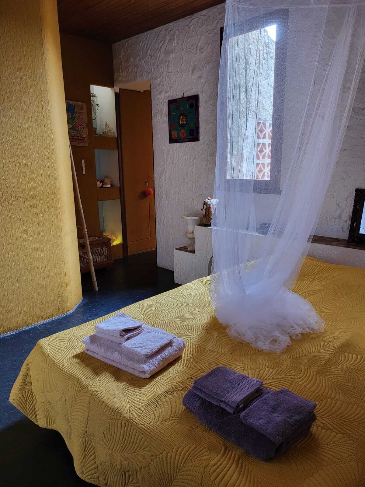 A room with a bed covered by a white canopy, a yellow textured bedspread, and two towels (one pink, one purple) on the bed.