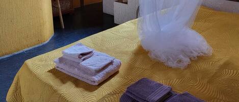 A room with a bed covered by a white canopy, a yellow textured bedspread, and two towels (one pink, one purple) on the bed.
