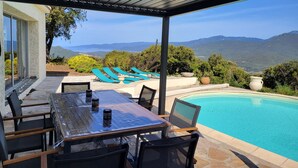 Un espacio al aire libre techado con piscina, sillas de descanso y una mesa con sillas.