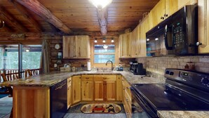 A rustic cabin-style kitchen with wooden cabinets, a granite countertop, a built-in stove, and a large window. - Spencer View (Waterfront on Moosehead Lake with Mountain Views) (Greenville)