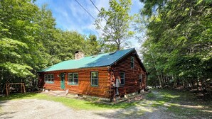 A log cabin with a green roof, surrounded by dense forest. - Spencer View (Waterfront on Moosehead Lake with Mountain Views) (Greenville)