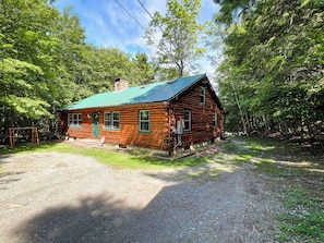 A log cabin with a green roof, surrounded by dense forest.