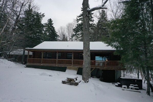 Une cabane en rondins avec une terrasse, entourée d’un paysage enneigé et d’arbres.