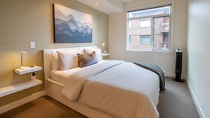 A bedroom with a bed, bedside tables, a wall-mounted artwork, a window, and a radiator. - Mt. Tolmie View-Spacious, Bright NE Facing Two Bedroom Condo with Den by Victoria Prime! (Victoria)