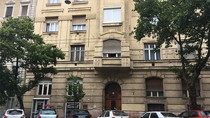 Ein mehrgeschossiges Gebäude mit einem zentralen Eingang, mehreren Fenstern und geparkten Autos davor.