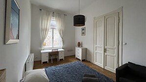 Ein Schlafzimmer mit einem Bett, einem Schreibtisch, einem Stuhl, einem Kleiderschrank und einem schwarzen Sessel.