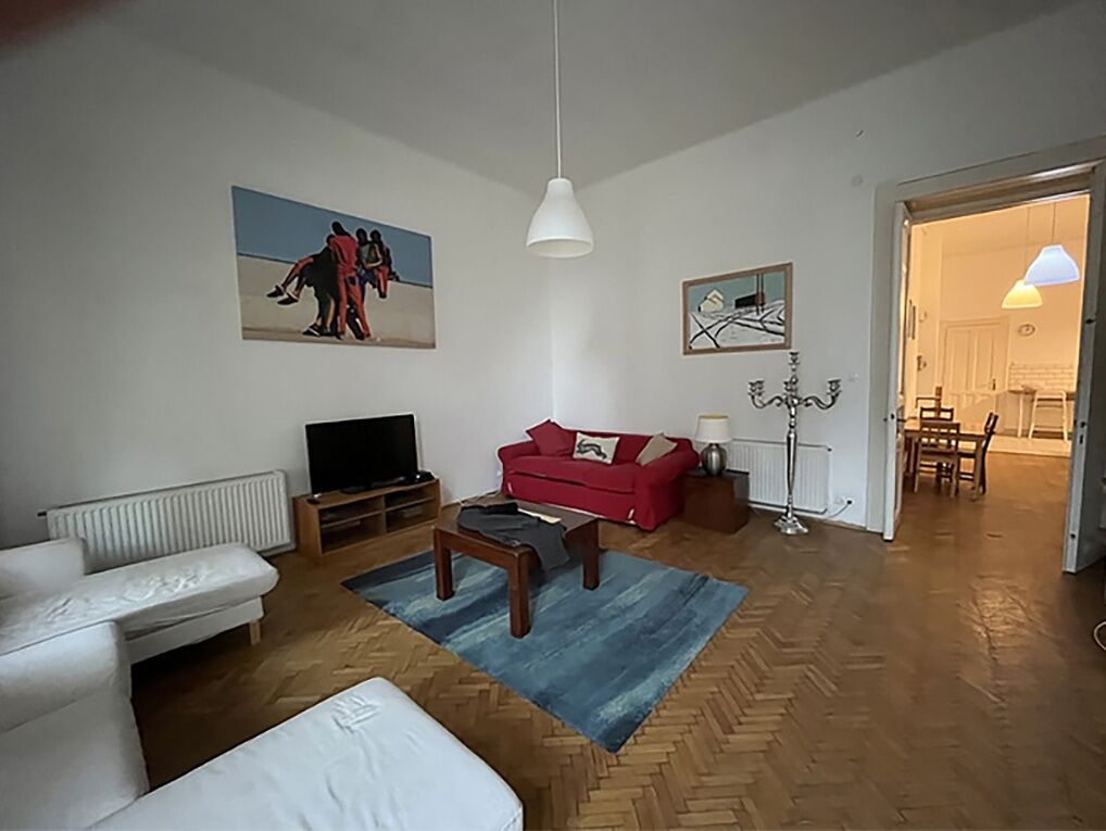 A living room with a white sofa, a red sofa, a TV, and artwork on the walls.