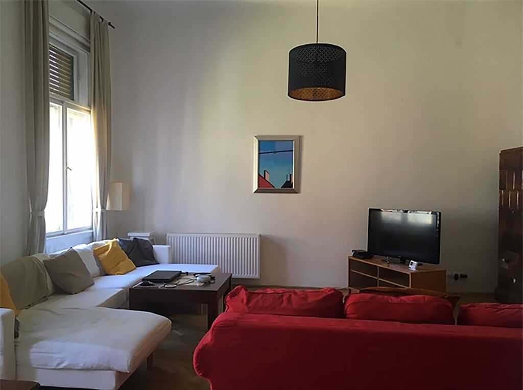 A living room with a white sofa, a red sofa, a television, and a hanging lamp.
