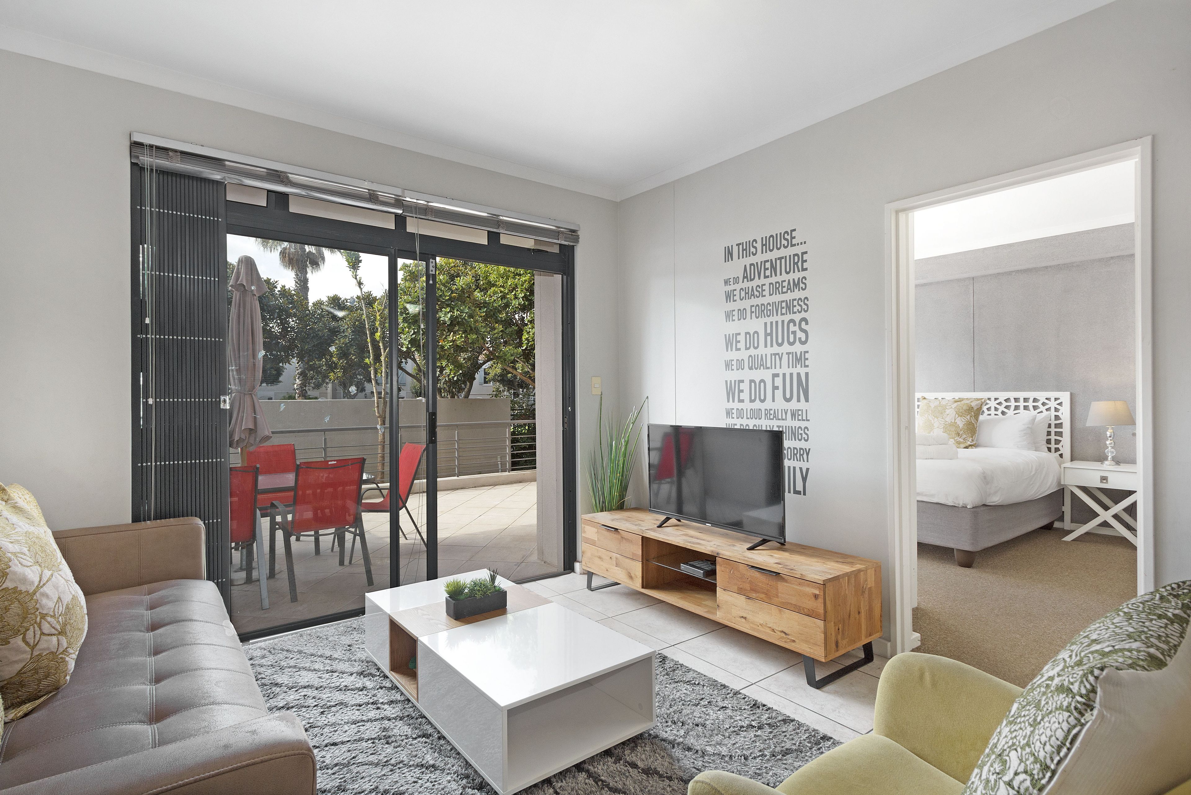 A modern living room with a sofa, coffee table, TV, and a balcony with red chairs.