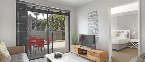 A modern living room with a sofa, coffee table, TV, and a balcony with red chairs.