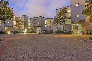 A multi-story residential building with balconies, a paved driveway, and potted plants. - Waterstone East C103 (Cape Town)
