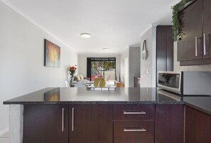 A modern kitchen with dark wood cabinets, a granite countertop, and a dining area with a yellow chair. - Waterstone East C103 (Cape Town)