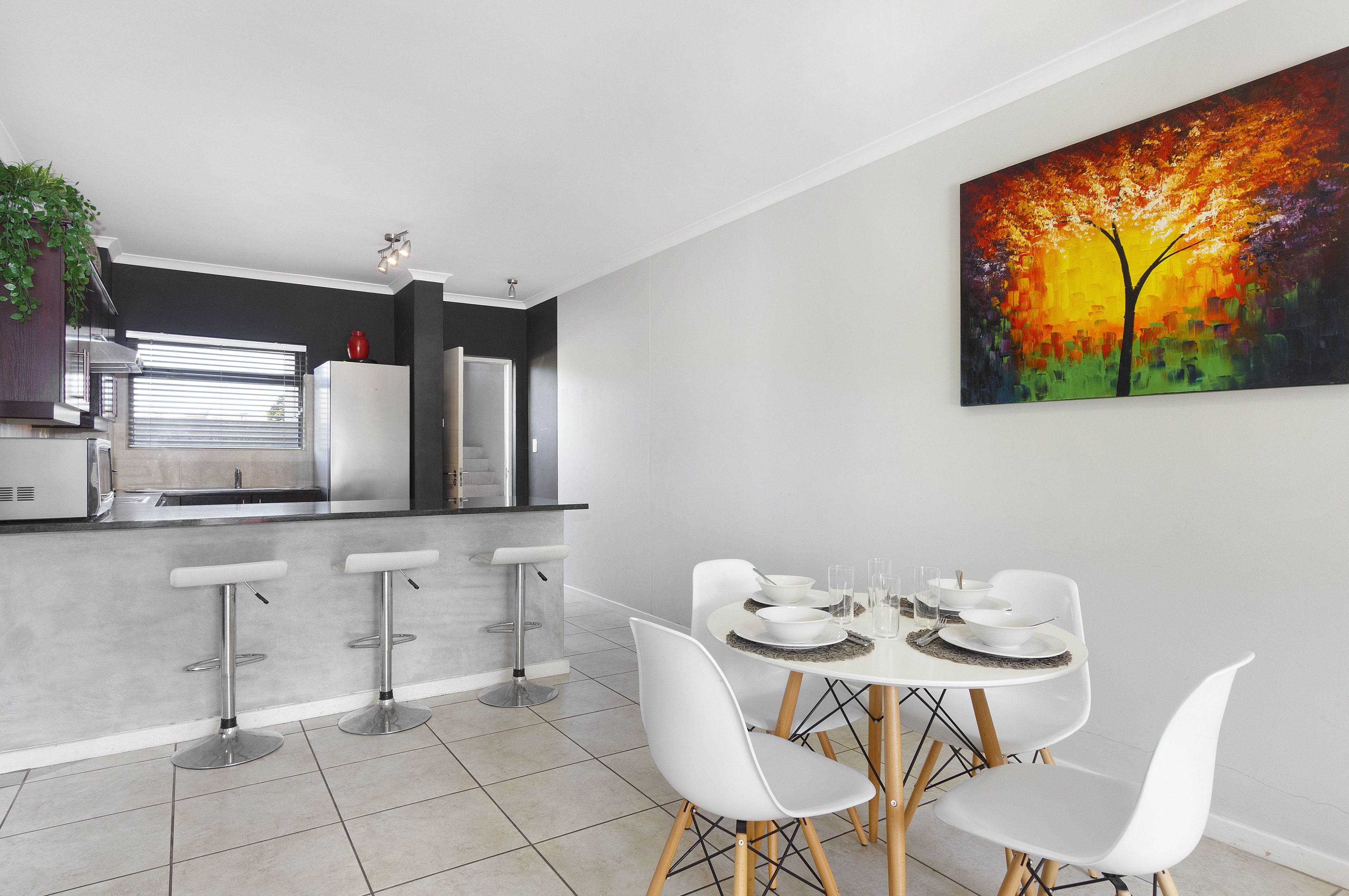 A modern kitchen with a dining area, including bar stools and a table set for four.