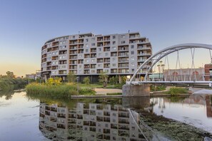 A multi-story residential building with balconies, a bridge, and a body of water reflecting the building. - Waterstone East C103 (Cape Town)