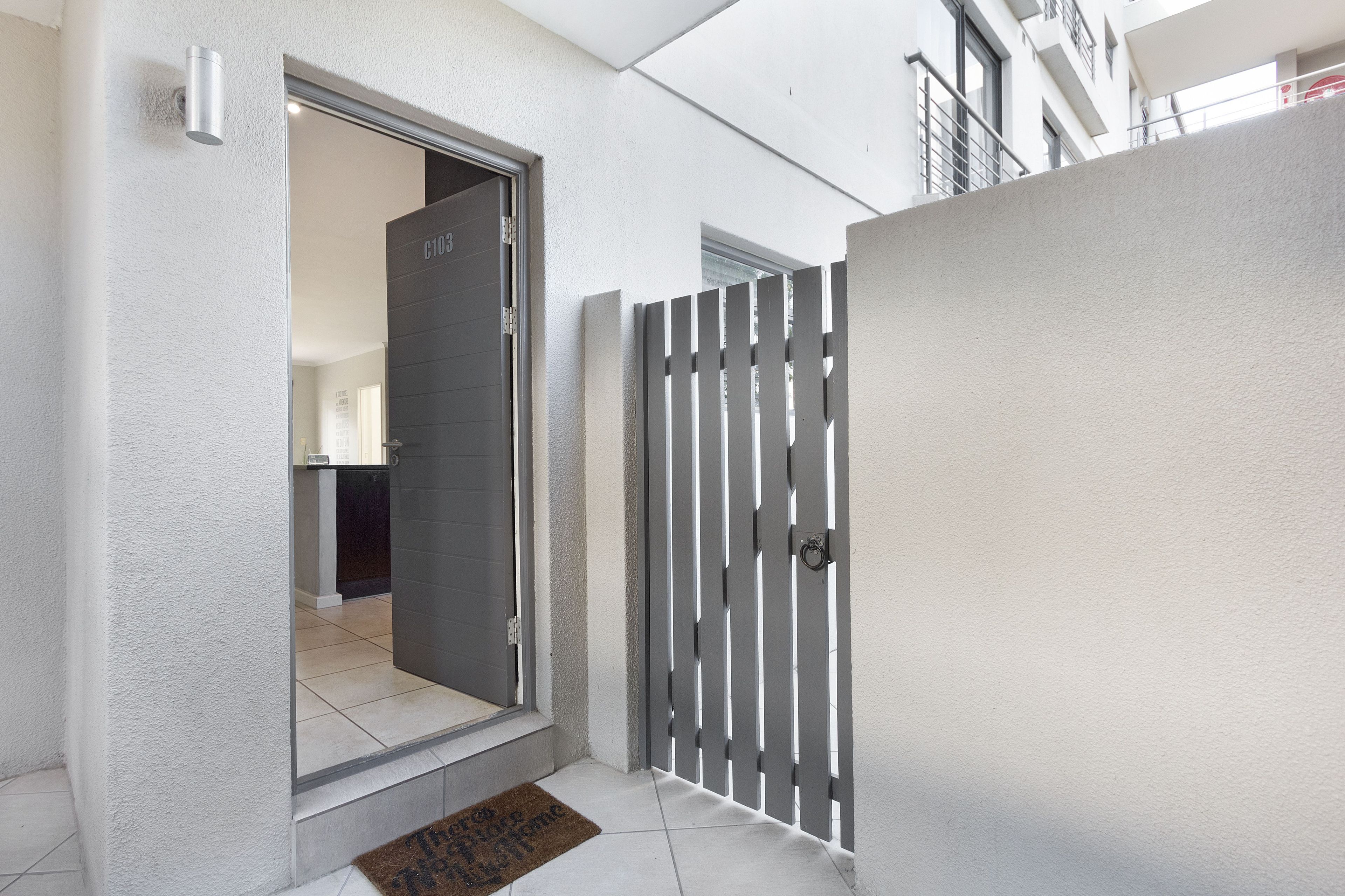 Entrada de un apartamento moderno con una reja metálica gris, una puerta a la vista y piso de baldosas.