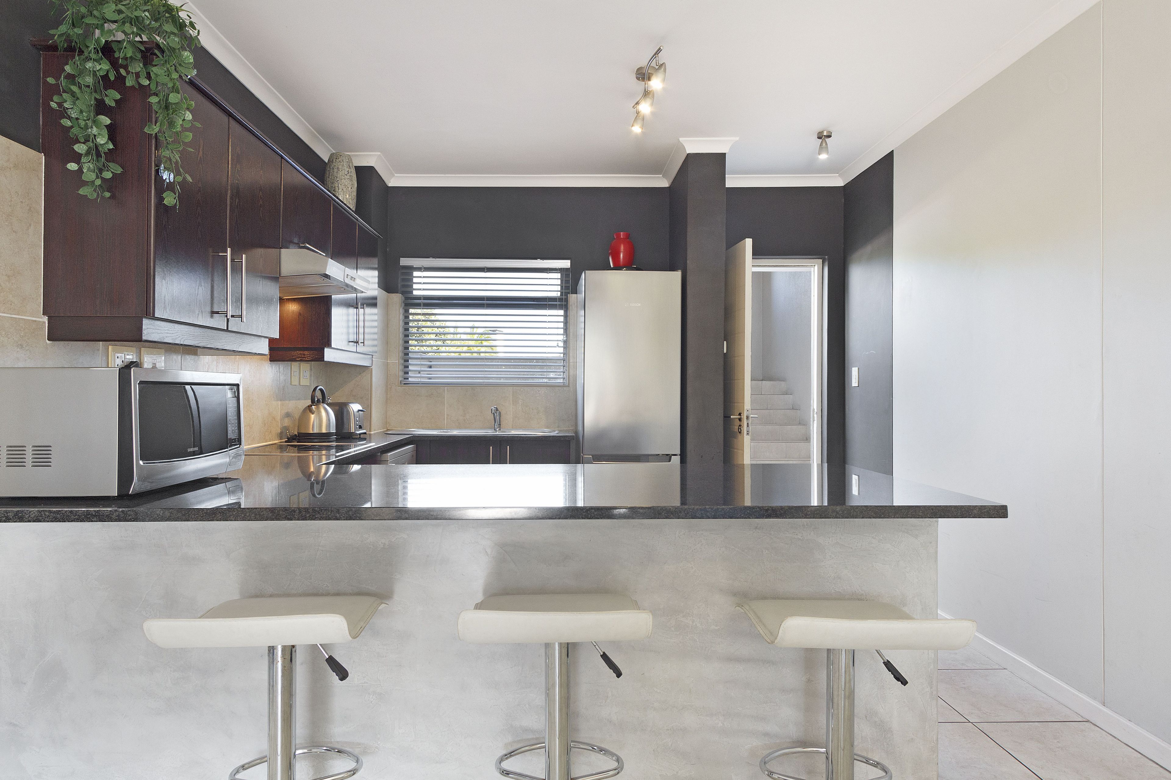 A modern kitchen with dark cabinetry, stainless steel appliances, and a central island with bar stools.