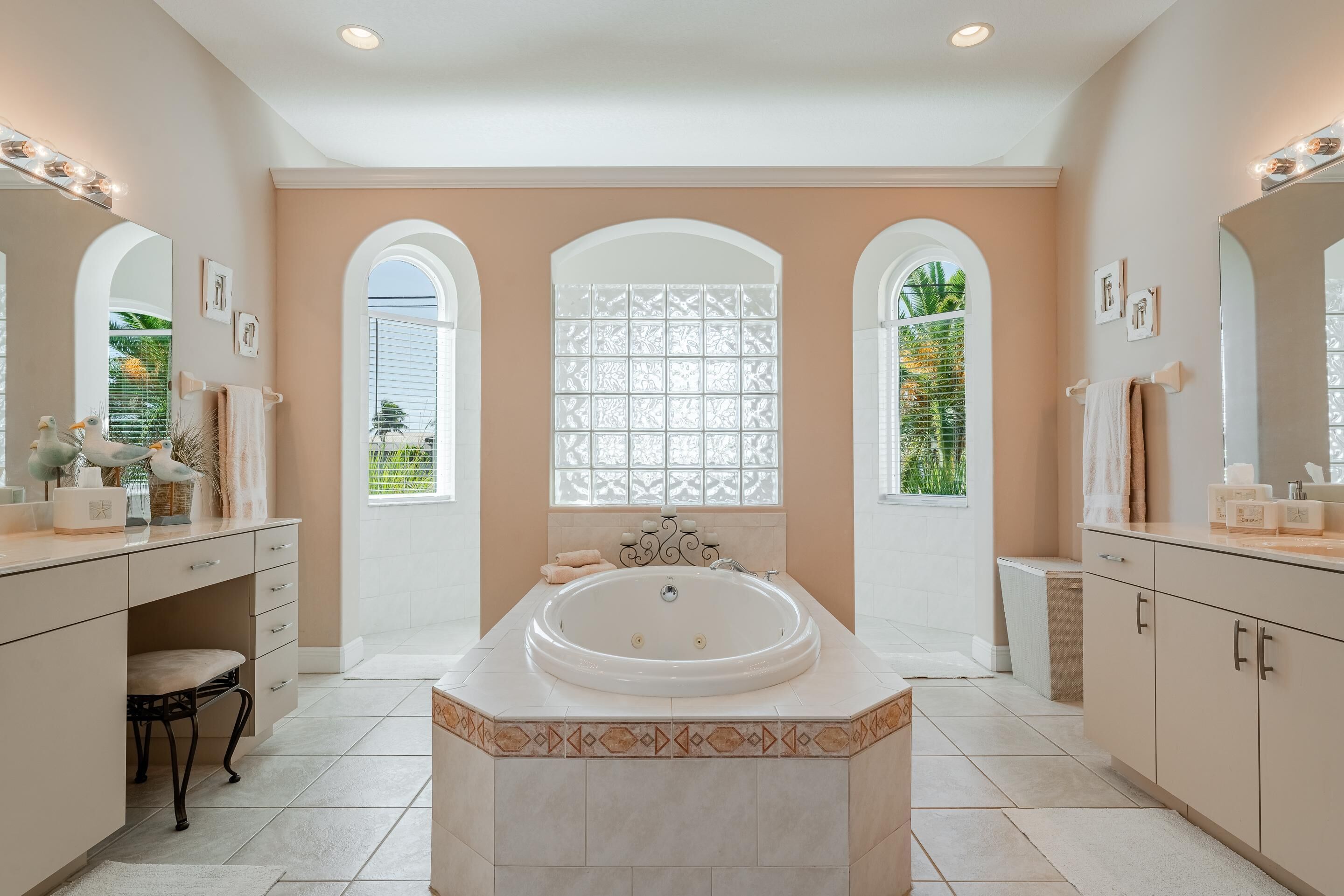 Un baño espacioso con una bañera grande, tocador con espejo y tres ventanas arqueadas.