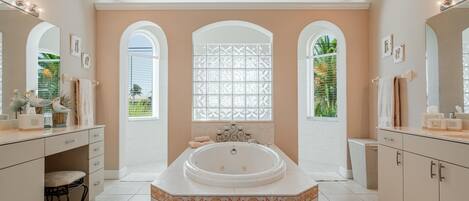 Un baño espacioso con una bañera grande, tocador con espejo y tres ventanas arqueadas.