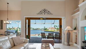 Ein Wohnzimmer mit beiger Couch, Couchtisch und Blick auf Pool und Außenbereich mit Sitzgelegenheiten.