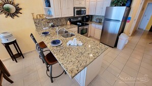 A kitchen with white cabinets, a granite countertop, a stainless steel refrigerator, and a microwave. - Sonoran Spa E603 - 2 BR Next to the Pool, High Speed Wi-Fi - Beachfront Upper Floor Luxury Condo (Puerto Peñasco)