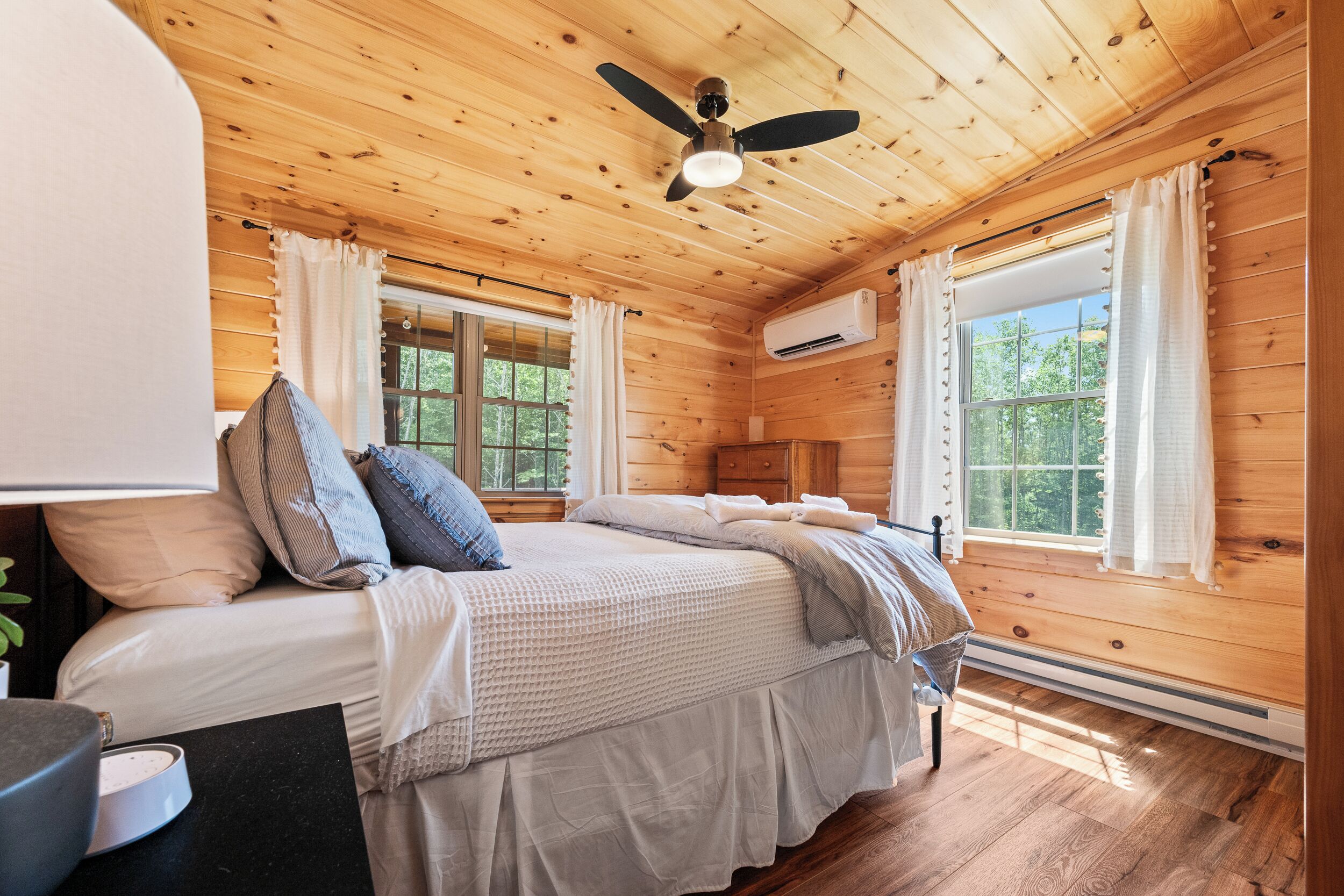 Ein Schlafzimmer einer Holzhütte mit Bett, Vorhängen, Klimaanlage und Deckenventilator.
