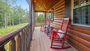 A wooden cabin with a porch featuring rocking chairs and a small table.