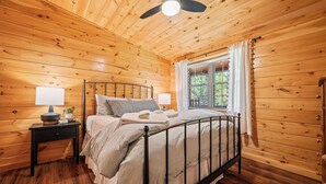 A wooden-paneled bedroom with a bed, bedside tables, a ceiling fan, and a window with curtains.