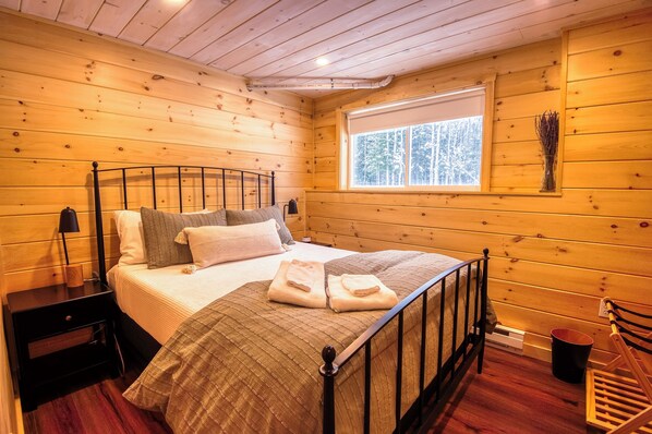 Un dormitorio de cabaña de madera con una cama, mesita de noche y ventana.