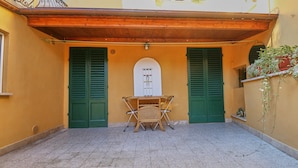 Un cortile con un tavolo e sedie, persiane verdi e pavimento in piastrelle.