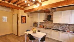 Una cucina con travi in legno, mobili bianchi, rivestimento in piastrelle e un tavolo da pranzo con sedie.