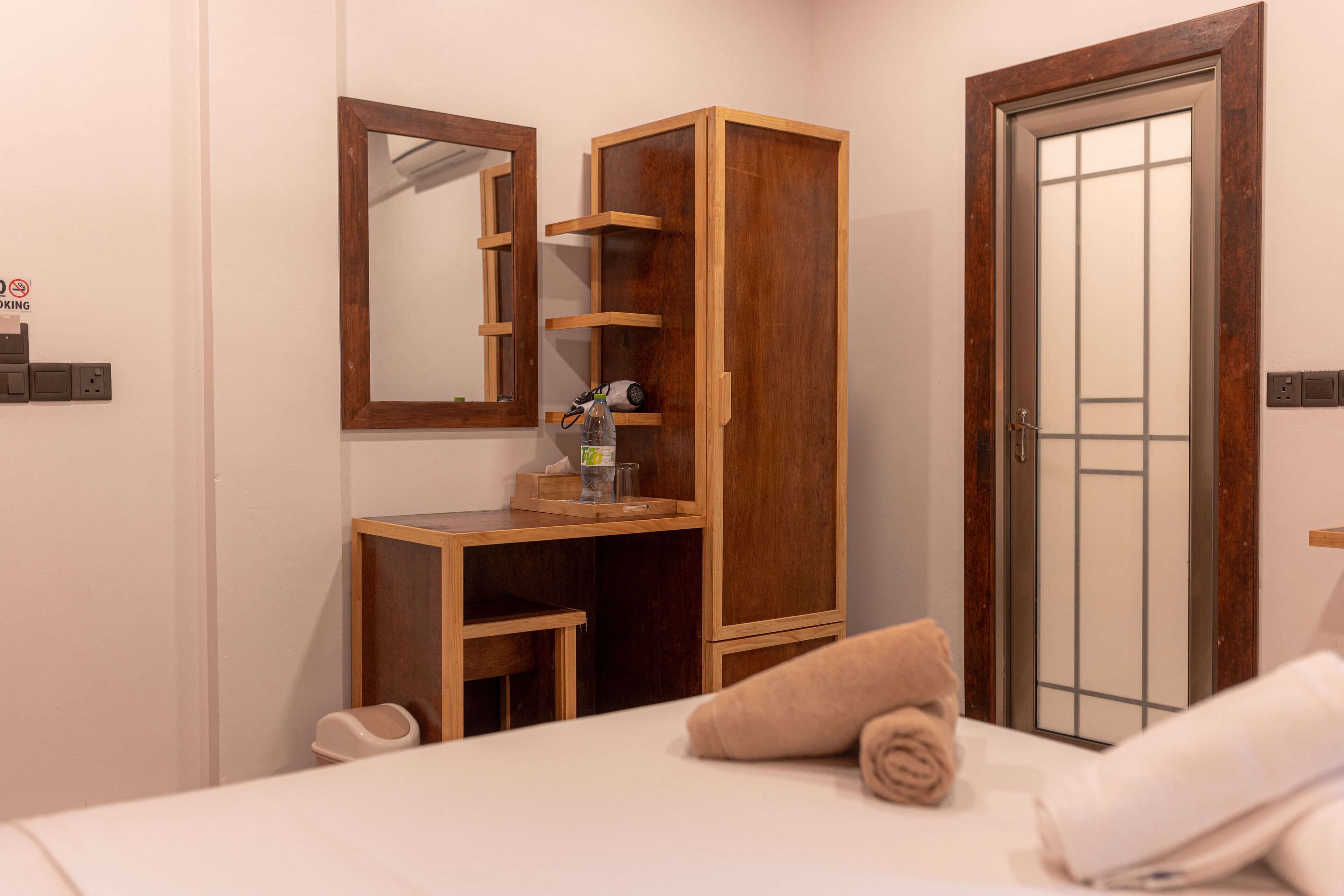 A hotel room with a wooden wardrobe, a mirror, a bed with towels, and a door with a frosted glass panel.