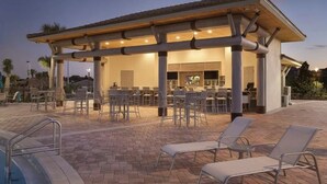 Un espace extérieur abrité, aménagé pour les repas, avec des chaises et des tables, une piscine et un bâtiment doté d’un toit en tuiles.