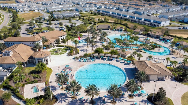 Vue aérienne d’un complexe hôtelier doté d’une grande piscine centrale, de plusieurs piscines plus petites, ainsi que de nombreux transats et parasols.