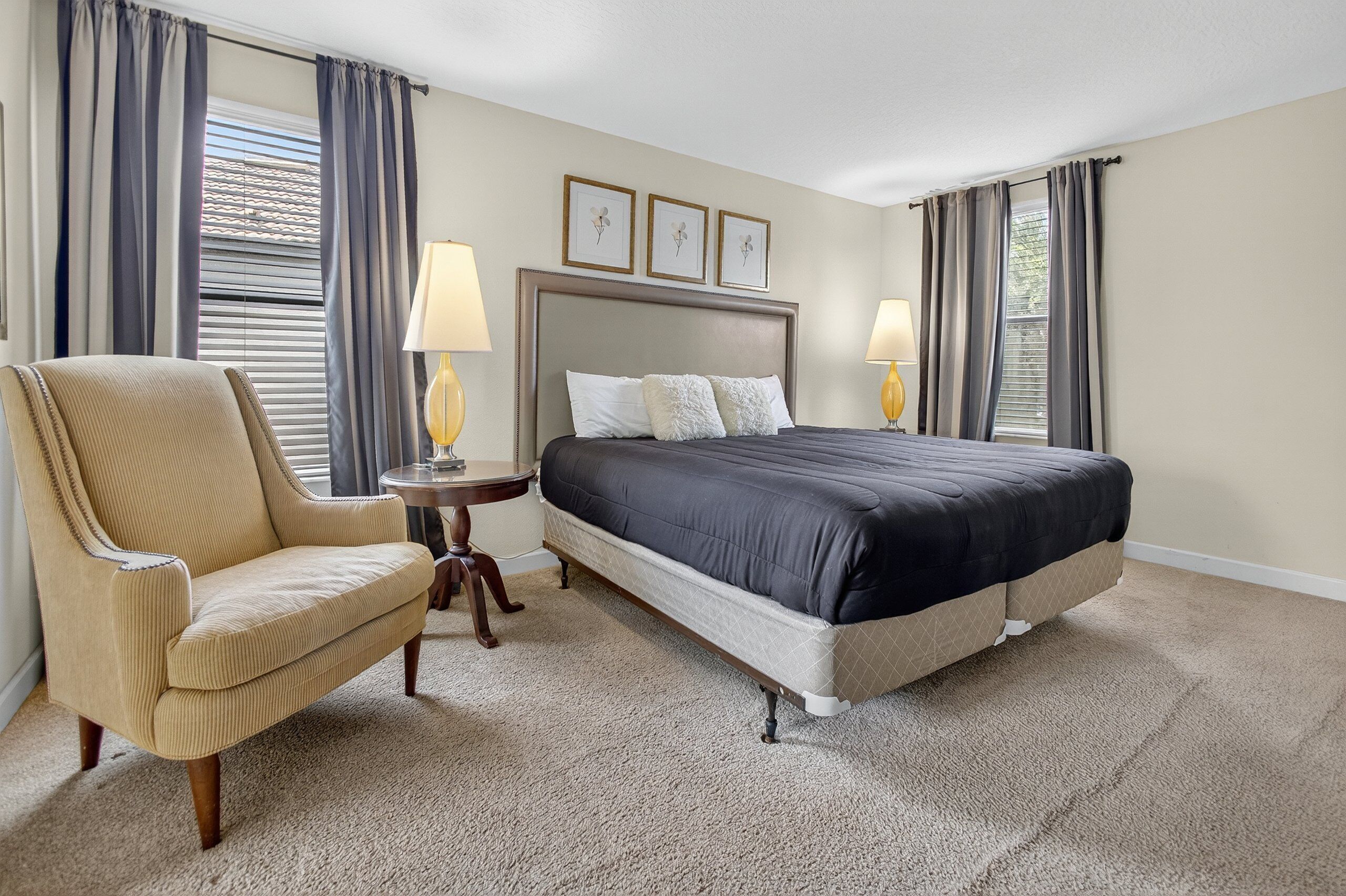 A bedroom with a large bed, a chair, two bedside tables with lamps, and three framed pictures on the wall.