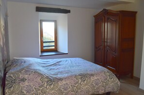 A bedroom with a bed, a window seat, and a wooden wardrobe.