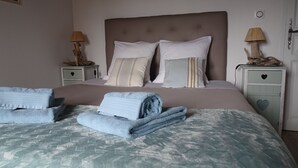 Una cama bien tendida con un edredón estampado, dos almohadas y dos toallas dobladas.