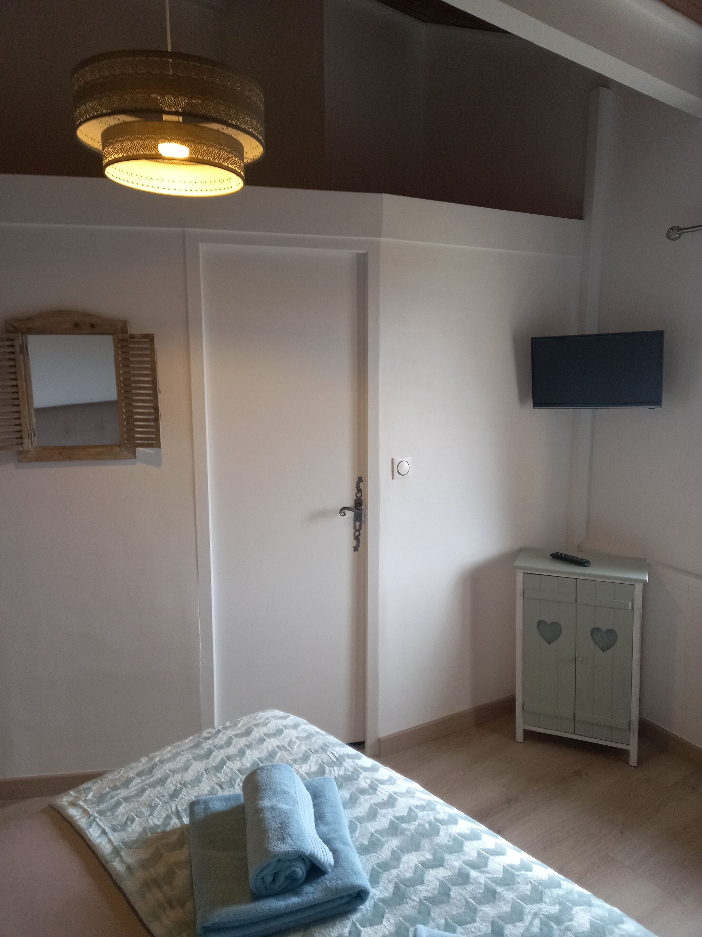 A bedroom with a bed, a bedside table, a television, a wardrobe, and a hanging light fixture.