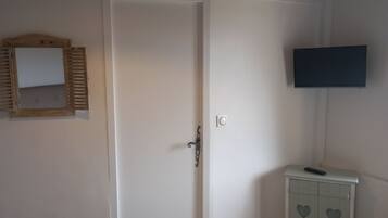 A bedroom with a bed, a bedside table, a television, a wardrobe, and a hanging light fixture.